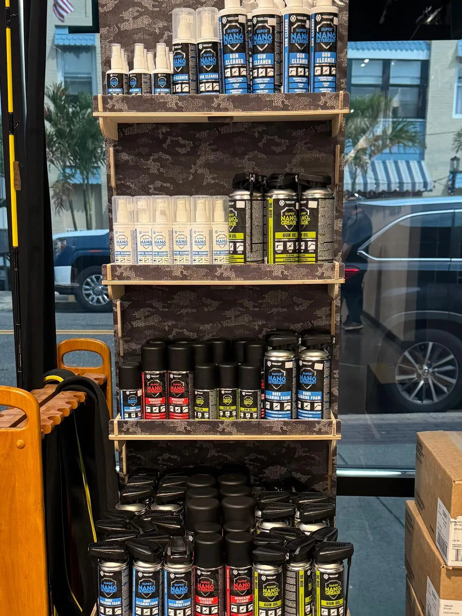 Four fully stocked shelves of GNP Defend gun cleaner, gun oil, grease, bore foam and optic cleaner on a floor display in a firearms retailer's storefront window